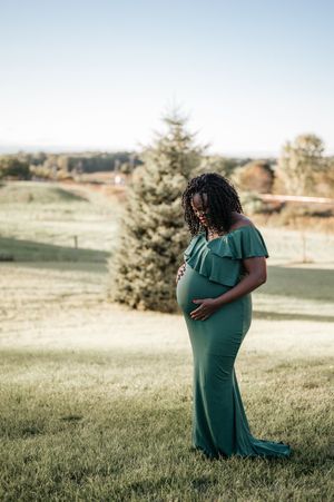 A maternity portrait in an emerald green dress against a scenic autumn landscape.