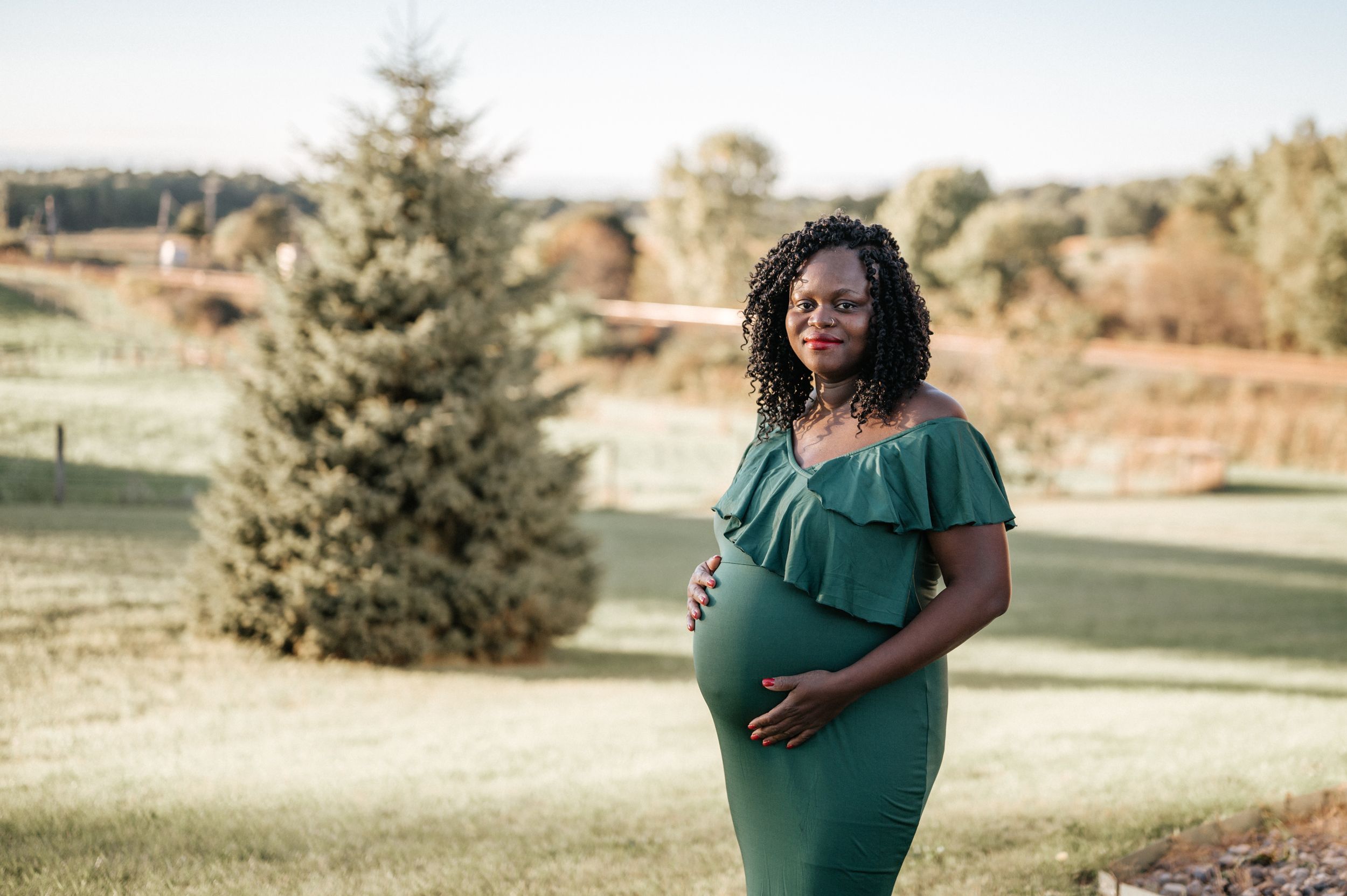 A serene outdoor maternity photo featuring a teal ruffle dress and natural scenery.