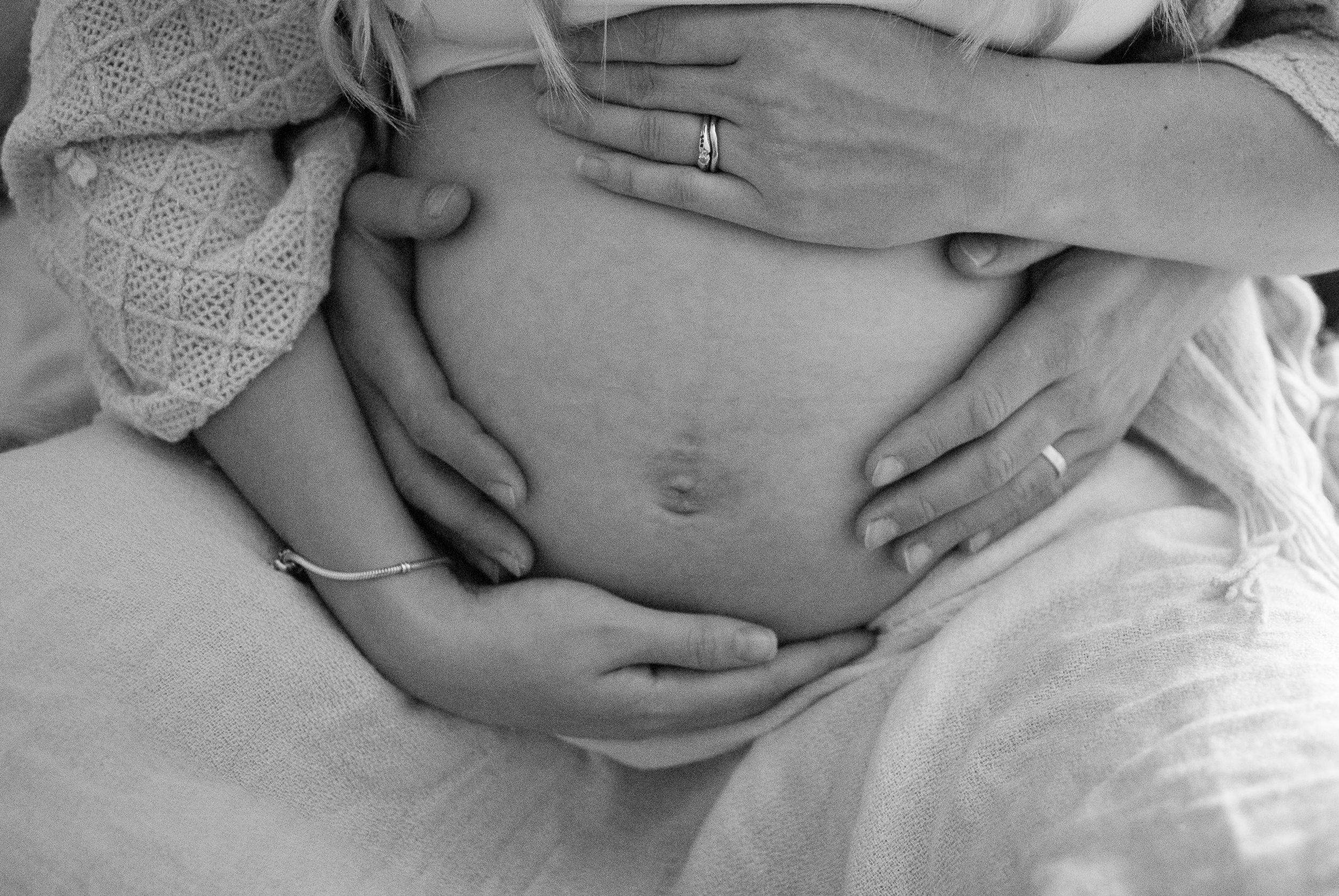 Close-up of intertwined hands resting on a pregnant belly during a maternity shoot by an in-home newborn photographer in Portland, Dorset