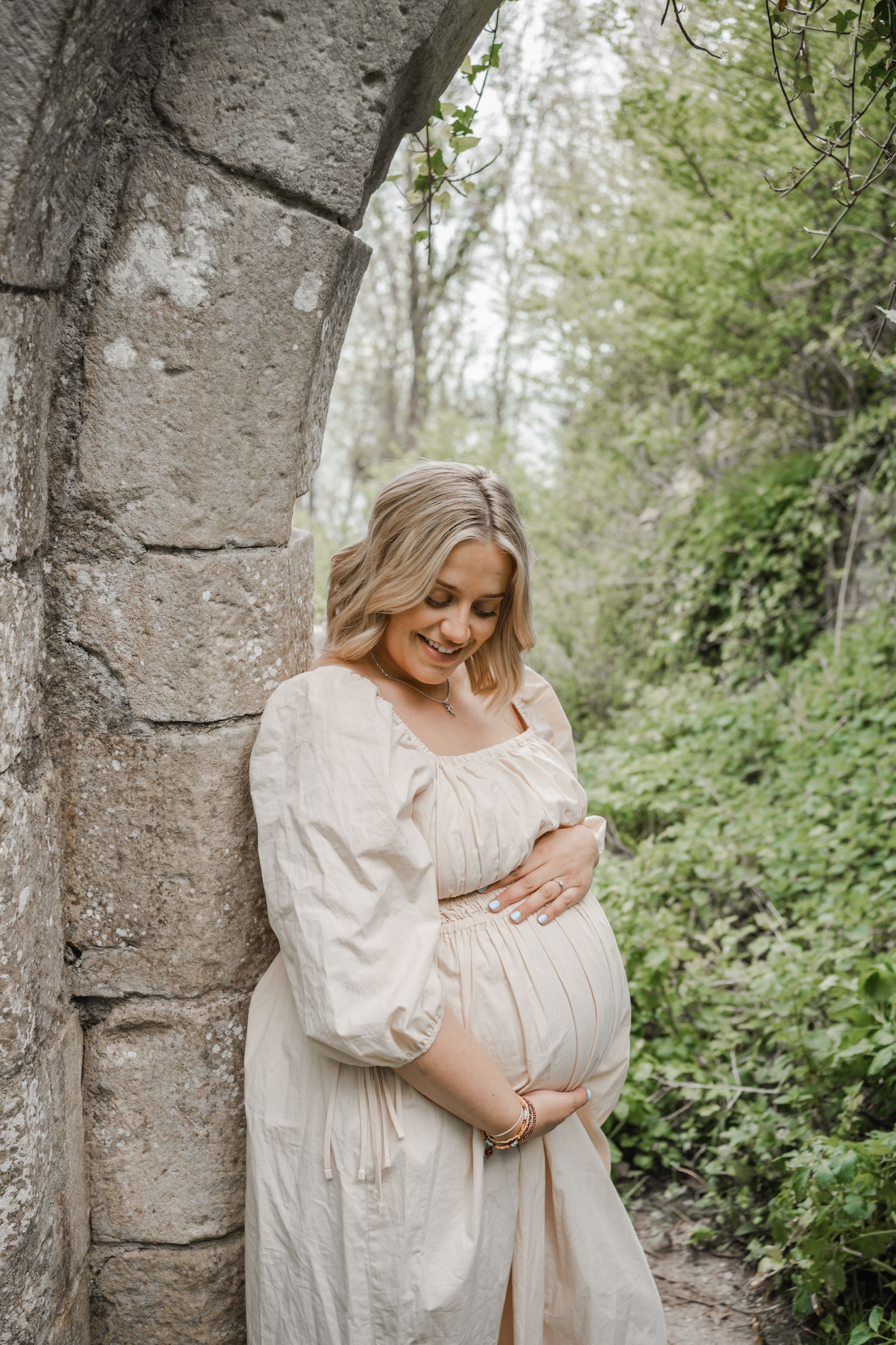 Pregnant woman poses for her photographer holding her bump during a natural light in-home and outdoor photoshoot in Portland, Dorset