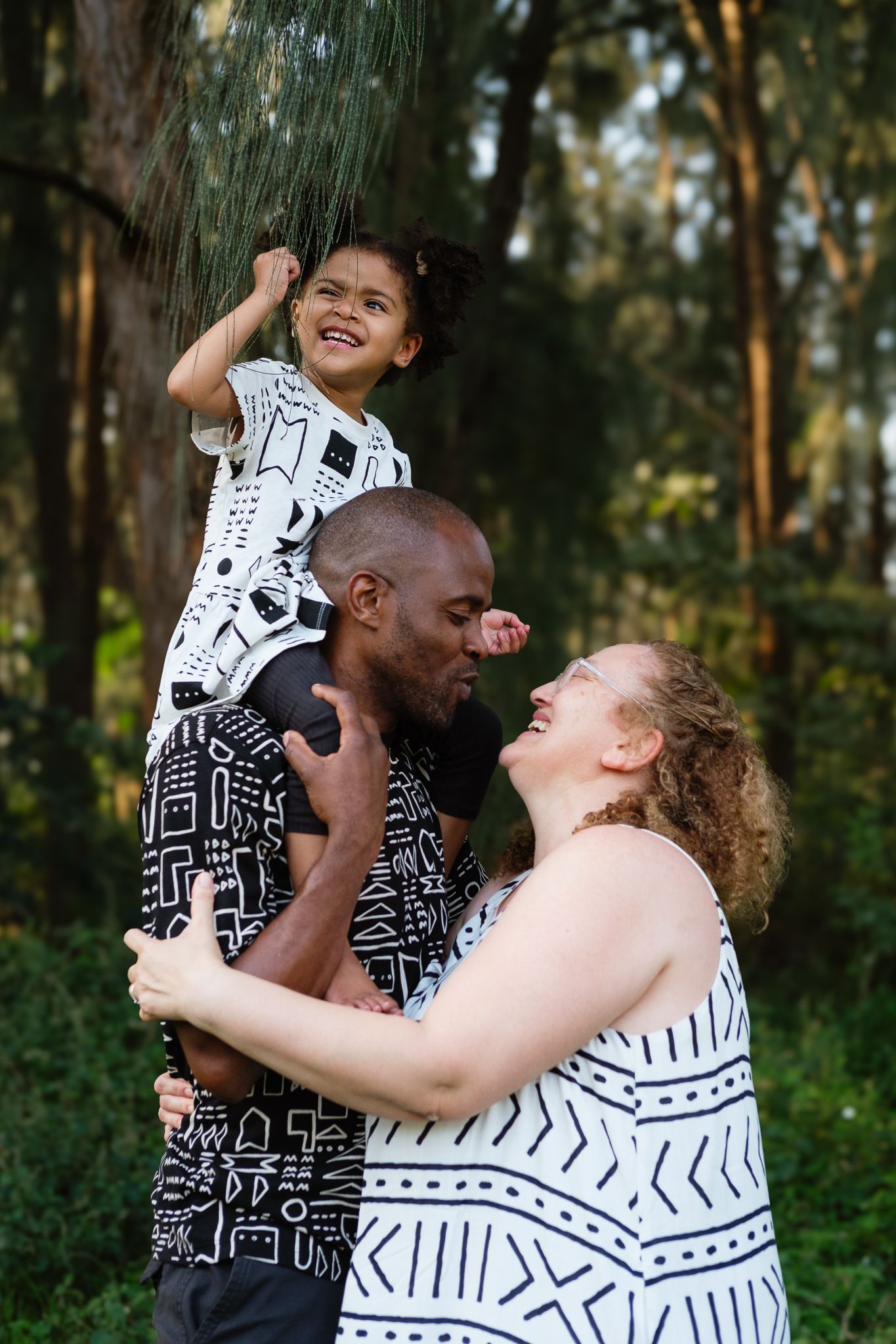 Family photoshoot with parents laughing while their daughter sits on dad’s shoulders