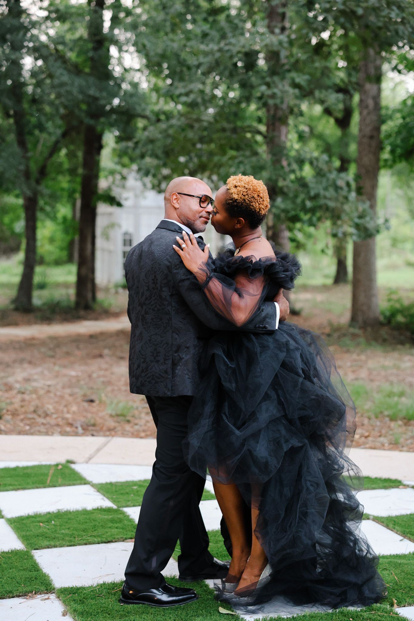 A couple sharing an intimate kiss moment on a checkerboard floor outdoors surrounded by trees in Texas