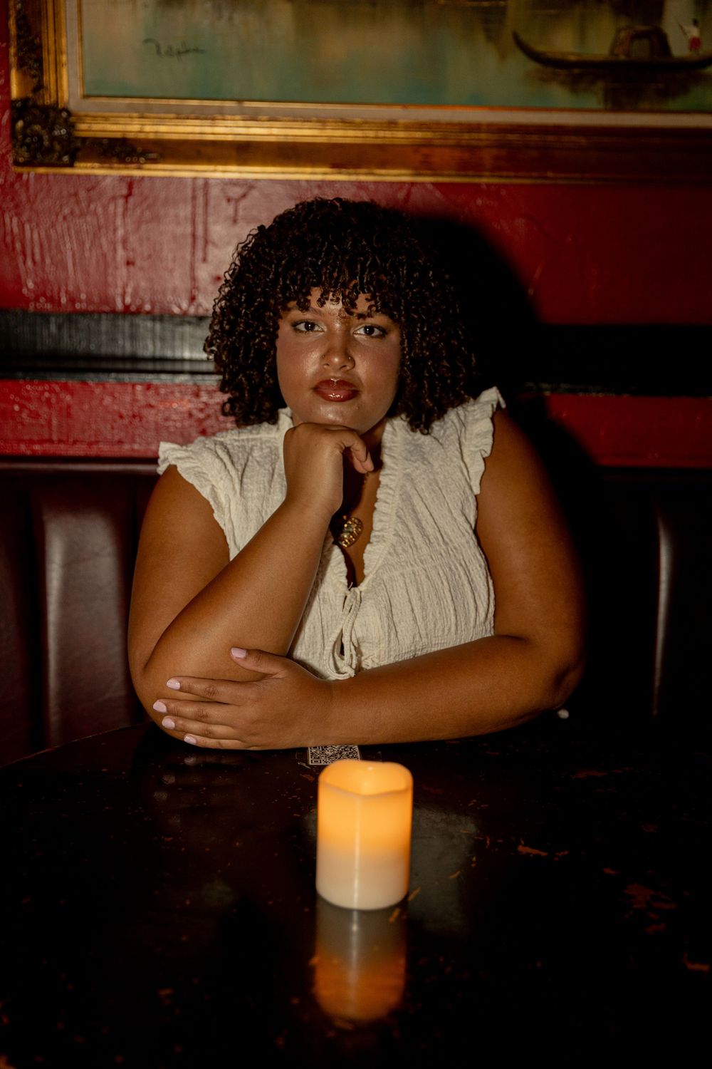 Person sitting at dimly lit bar with white top and candlelight creating intimate ambiance.