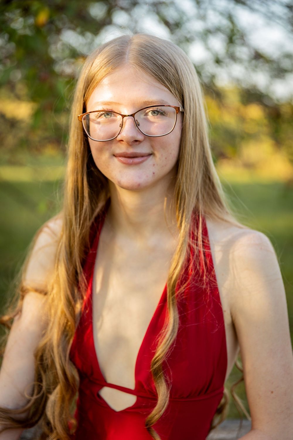 Portrait of someone in red dress and glasses against golden sunset background.