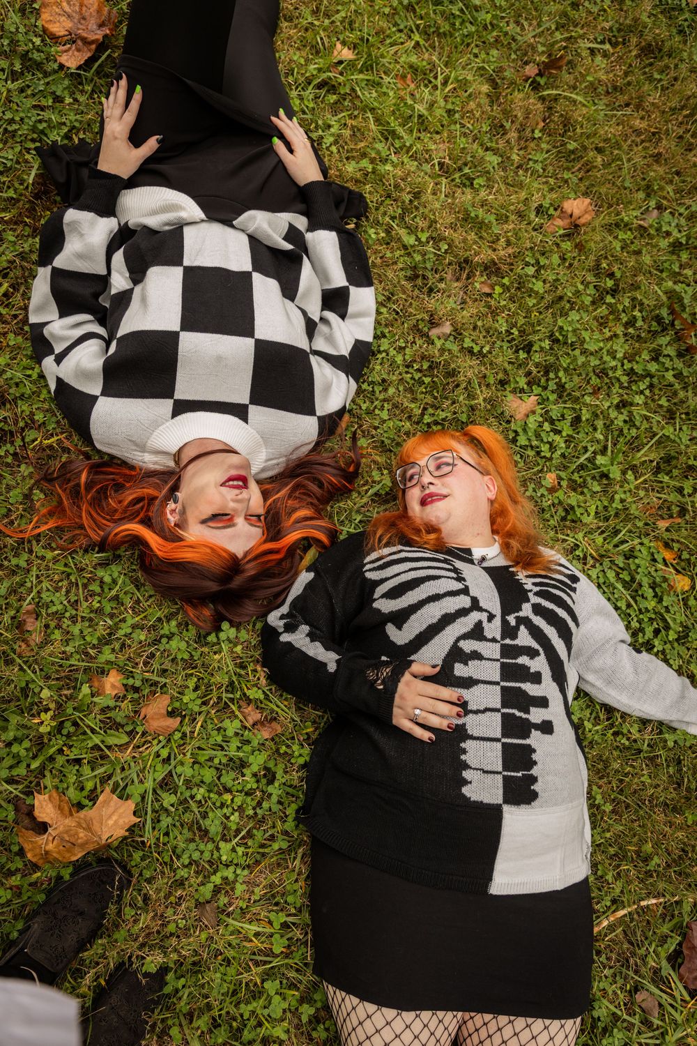 Two people lying on autumn grass in matching black and white checkered outfits.