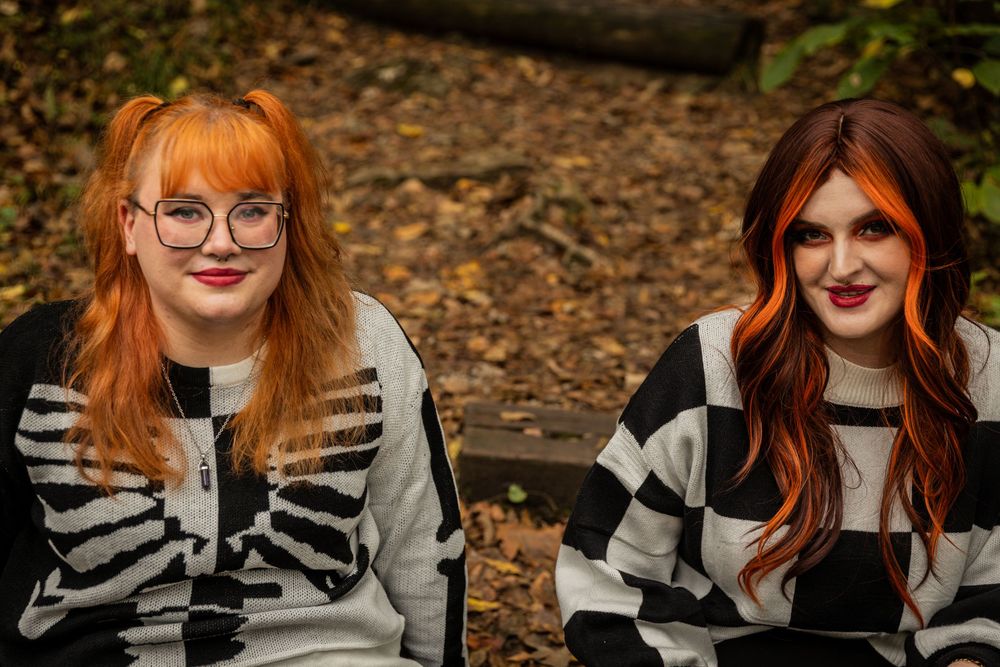 Two people in matching skeleton sweaters with vibrant hair sitting together outdoors.