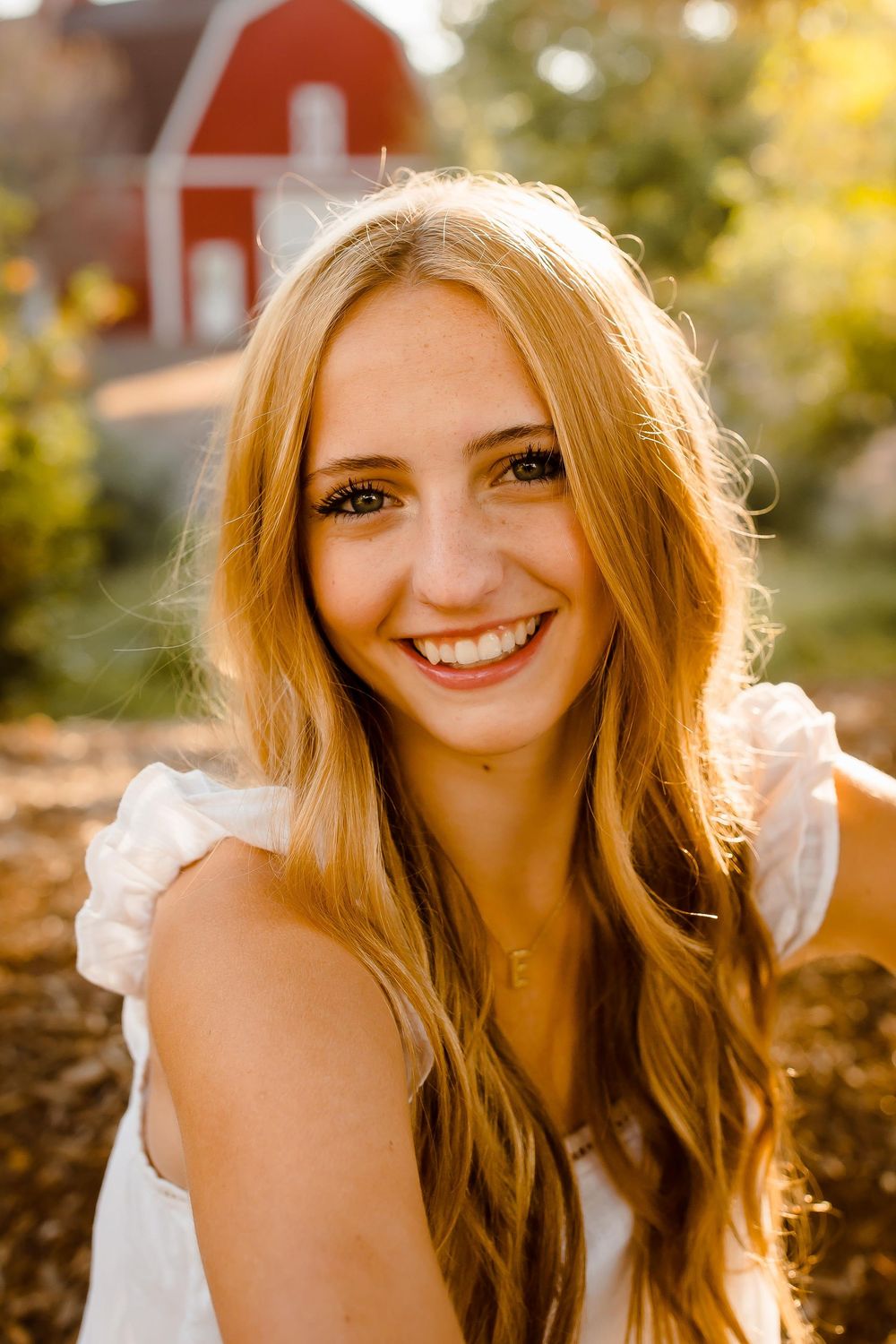 A high school senior smiles at golden hour in front of a barn in Littleton, Colorado
