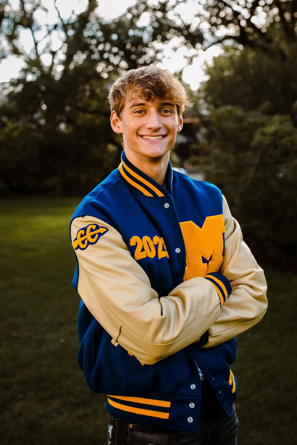 A high school senior smiles confidently in their letterman jacket at Wash Park in Denver