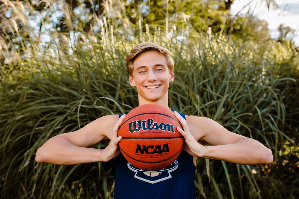 A high school senior smiles confidently with their basketball at Wash Park in Denver