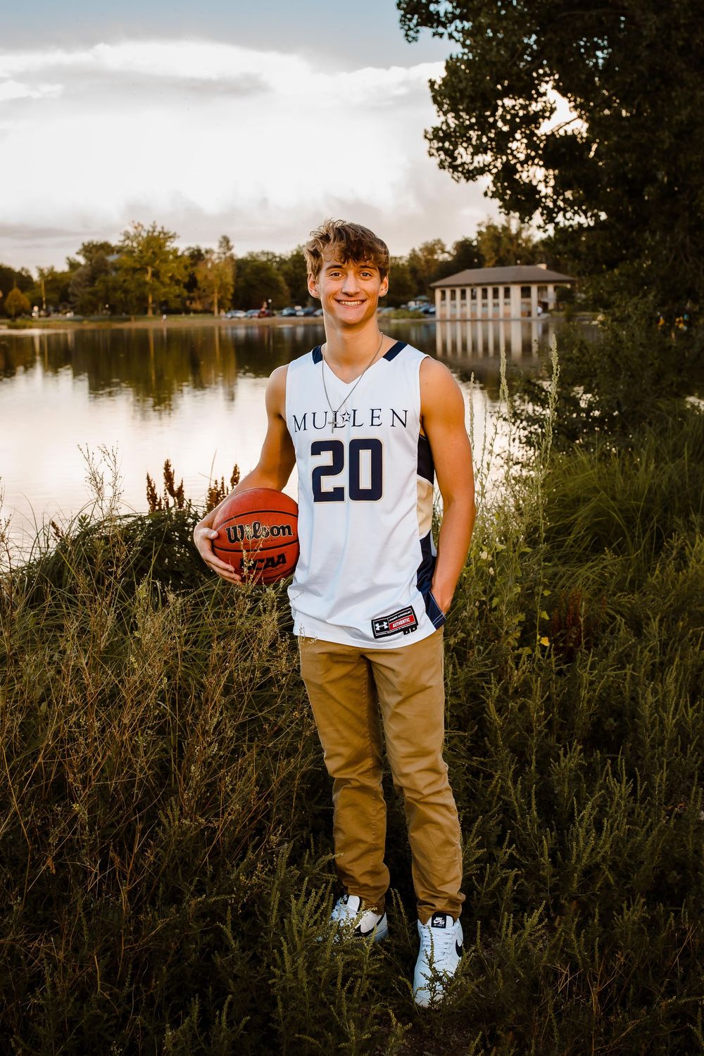 A high school senior smiles confidently with their basketball at Wash Park in Denver