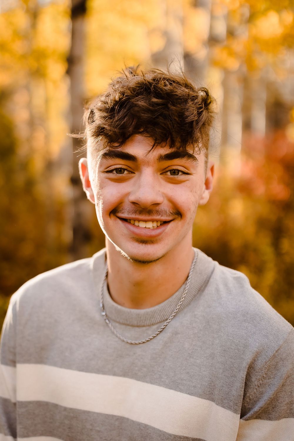 A teenager smiles in front of yellow aspens in Vail