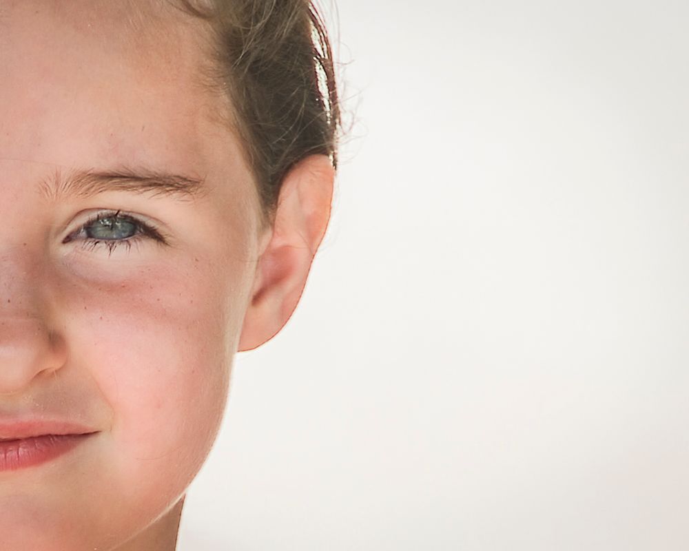 Close-up portrait of a young child with blue eyes and brown hair against a white background.