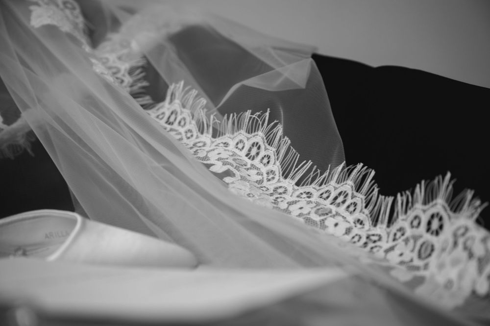 Close-up detail of intricate lace trim on wedding veil in black and white.