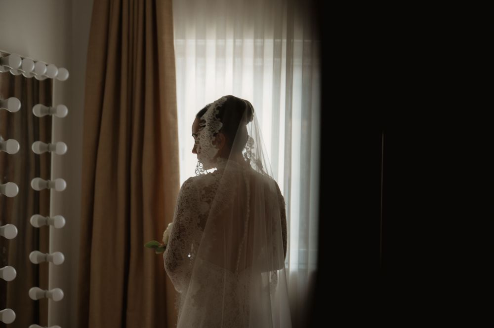 Silhouette of bride against window with vanity lights in background.