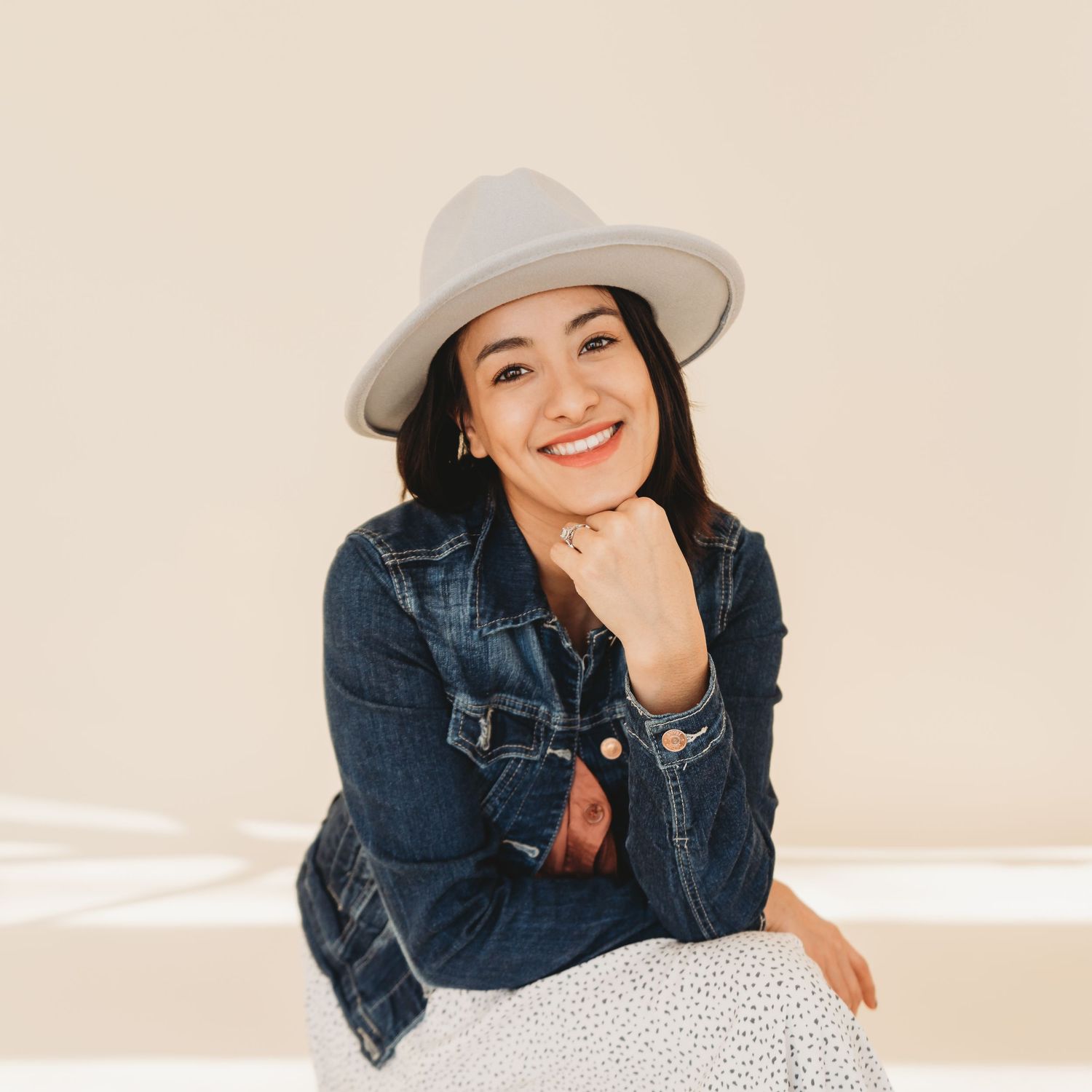 Portrait of someone wearing a denim jacket and grey fedora hat against a neutral background.