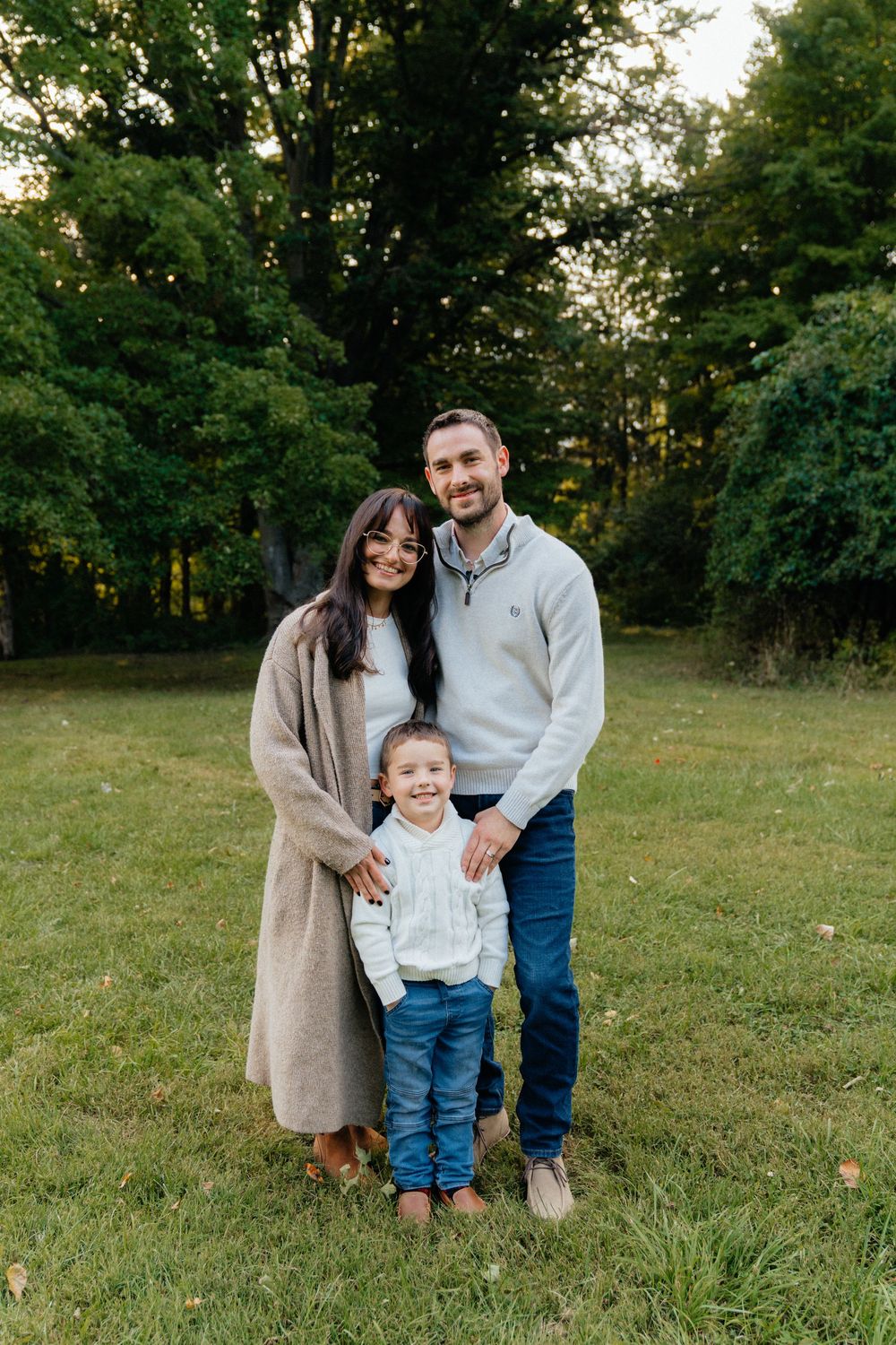 Family portrait in casual attire standing together on grassy field at sunset.