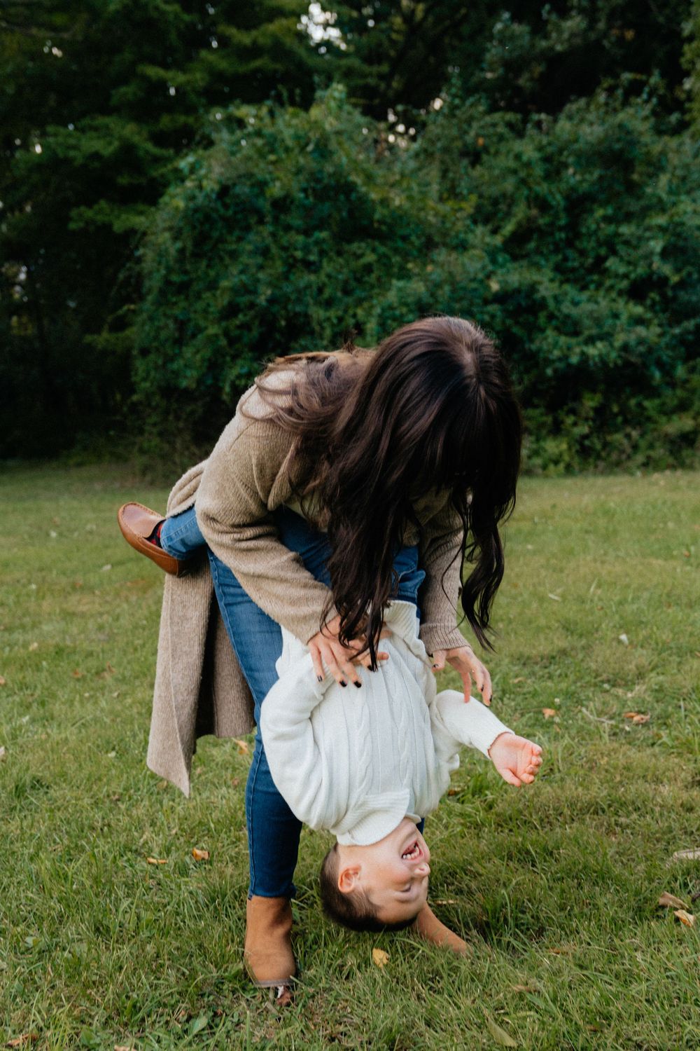 Playful family moment captured in outdoor setting with natural greenery backdrop.