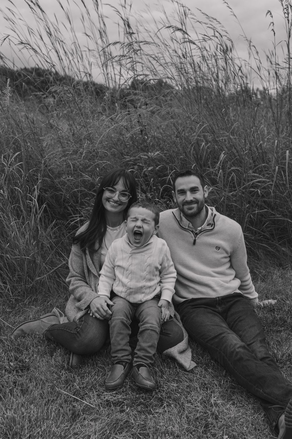 A black and white family portrait showing joyful expressions while lying in tall grass.
