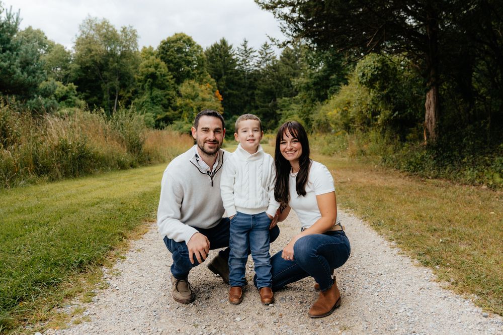 A family photo session on a gravel path surrounded by autumn trees.