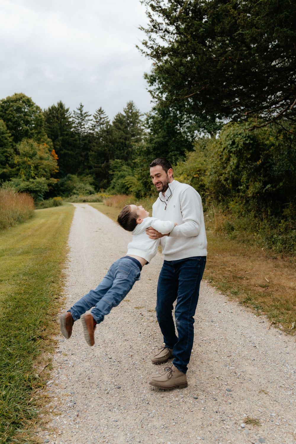Playful moments captured on a gravel trail as a child is swung through the air.