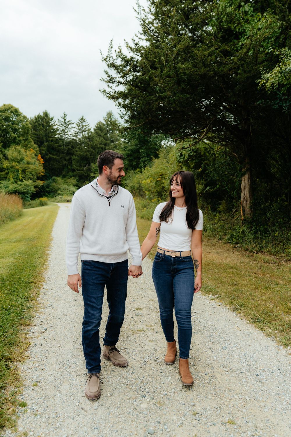 A couple walking hand in hand down a scenic gravel path surrounded by trees.