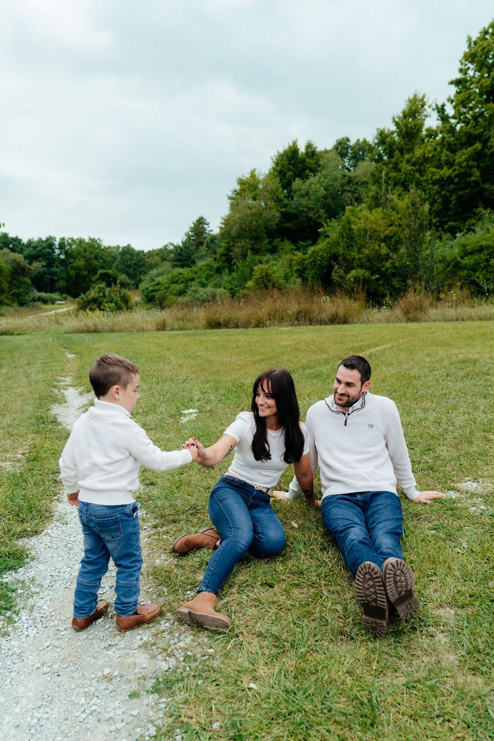 Family playing and laughing together while sitting on a grassy path outdoors.