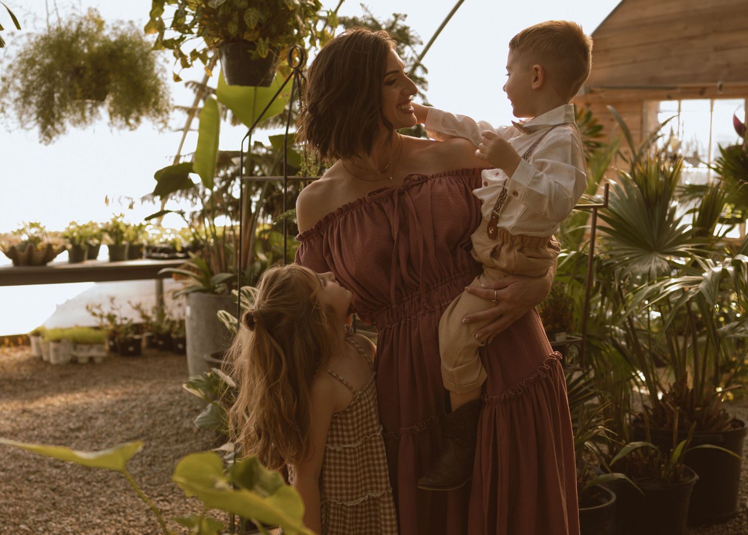 People gather among lush greenery in a greenhouse setting during golden hour.