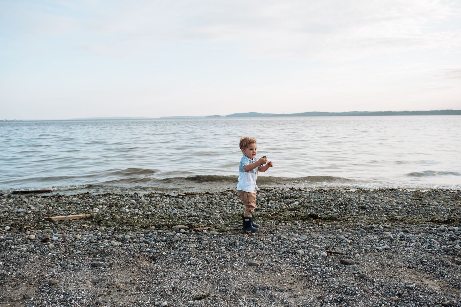 A small child plays on a rocky beach at sunset with water in the background.