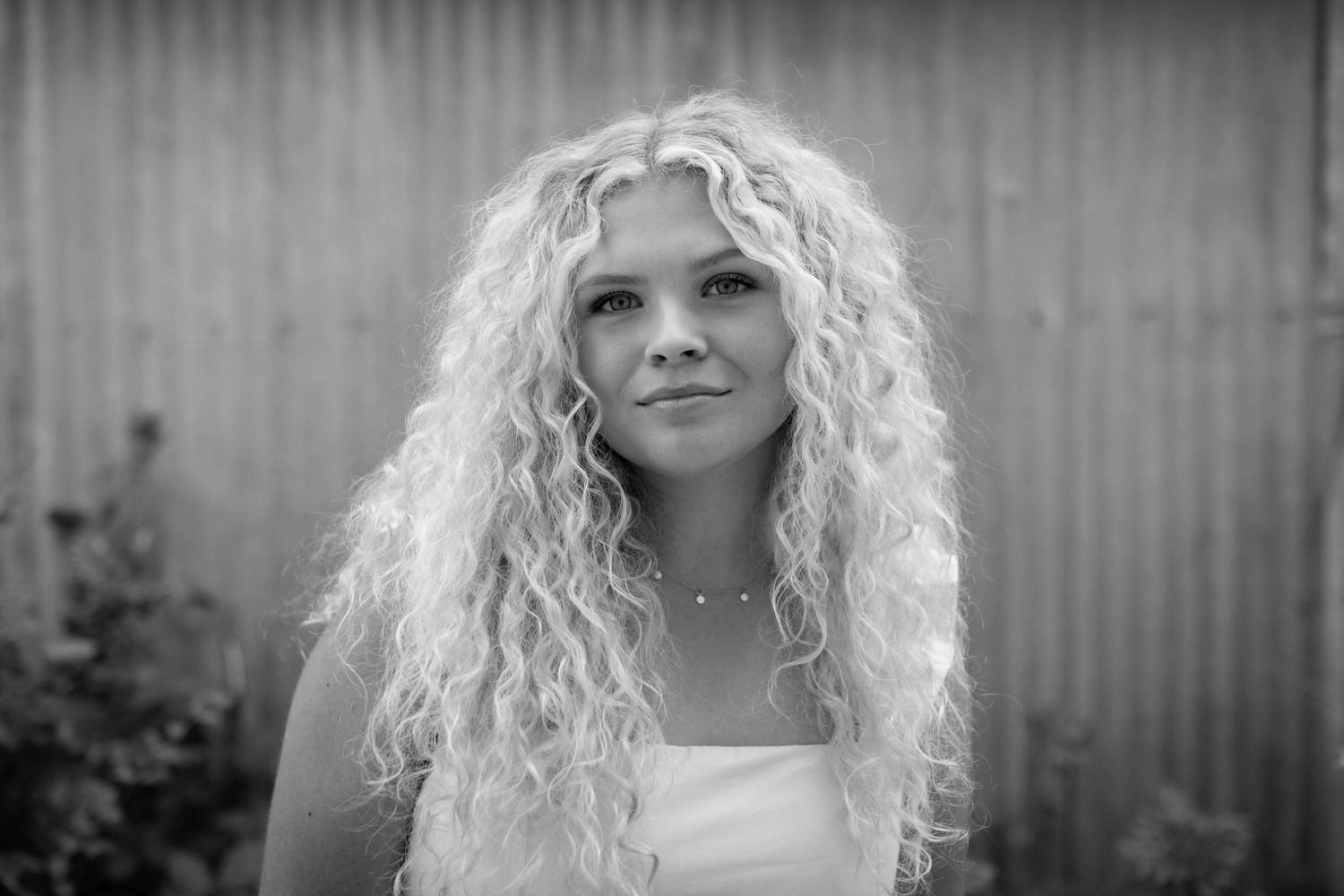 Black and white portrait of young woman with long curly blonde hair looking upward.