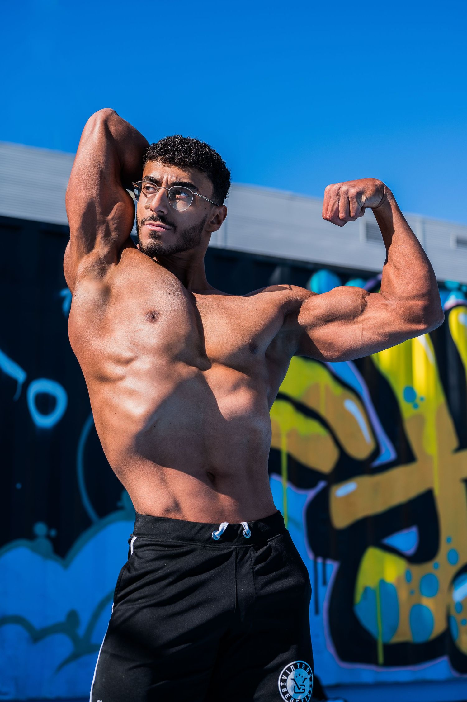 Fitness athlete demonstrating upper body muscles against urban graffiti wall.
