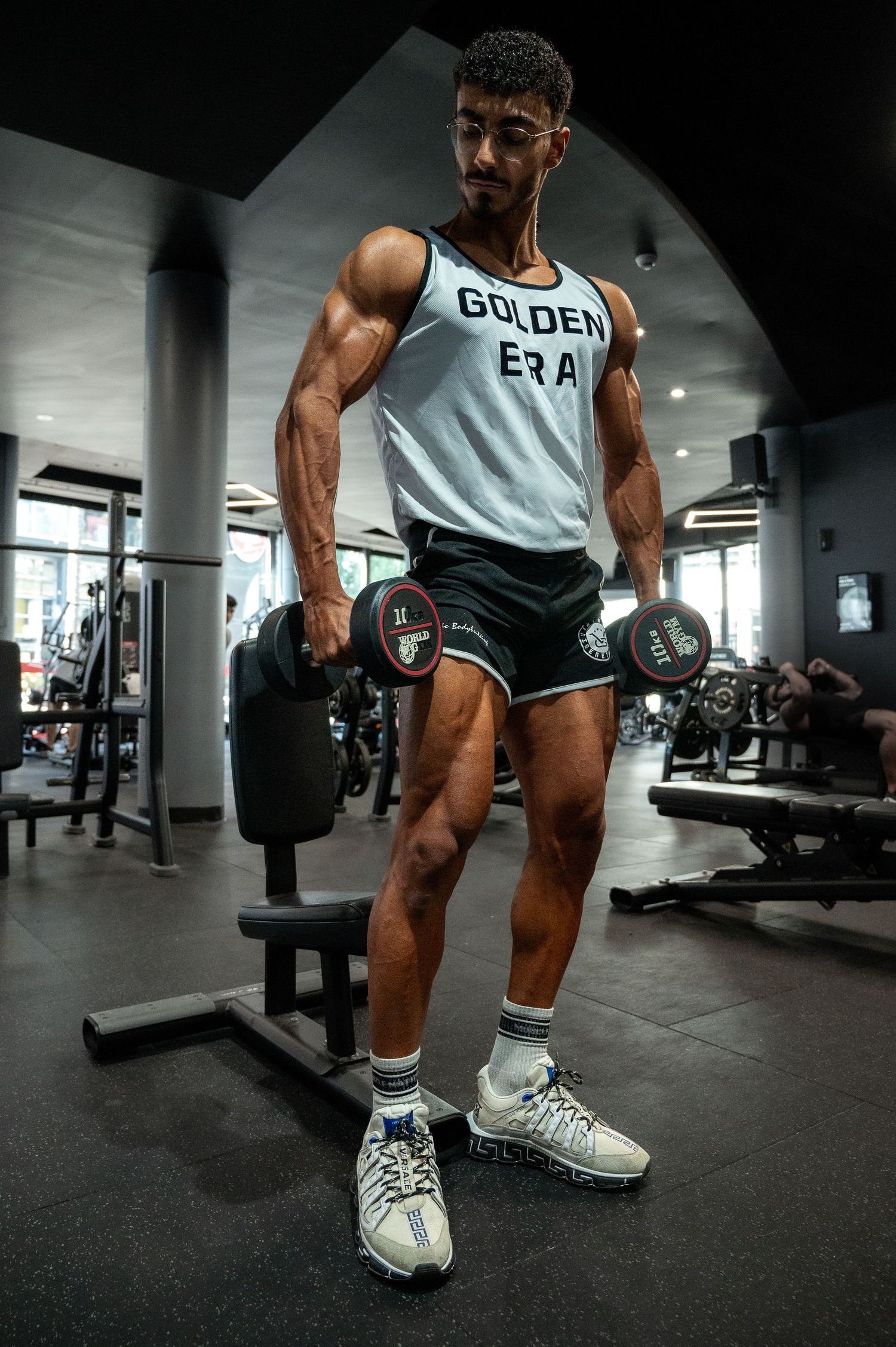 Muscular athlete in 'Golden Era' tank top performs dumbbell exercise at the gym.