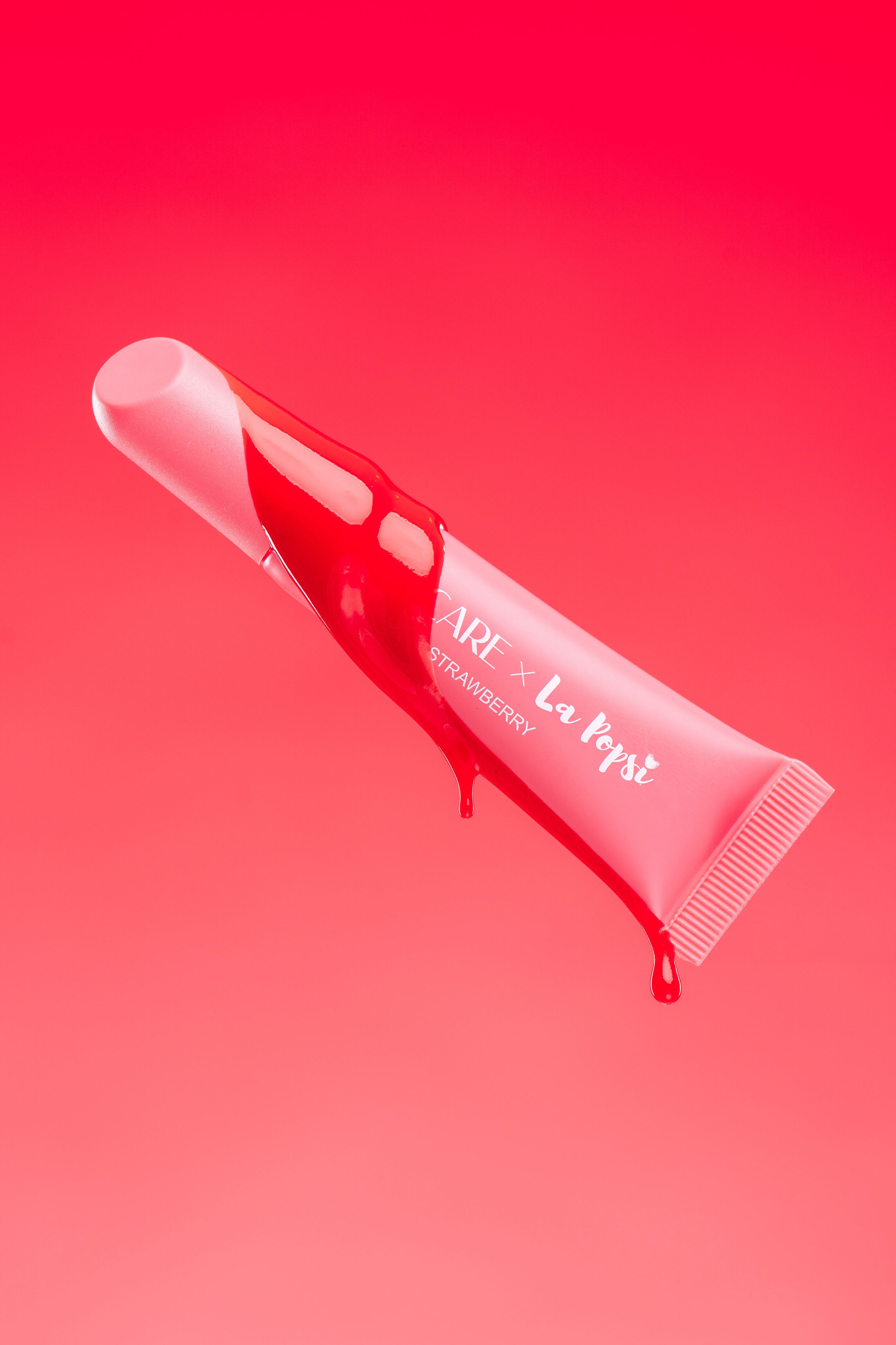 Beauty product tubes floating diagonally across a bright red gradient background.