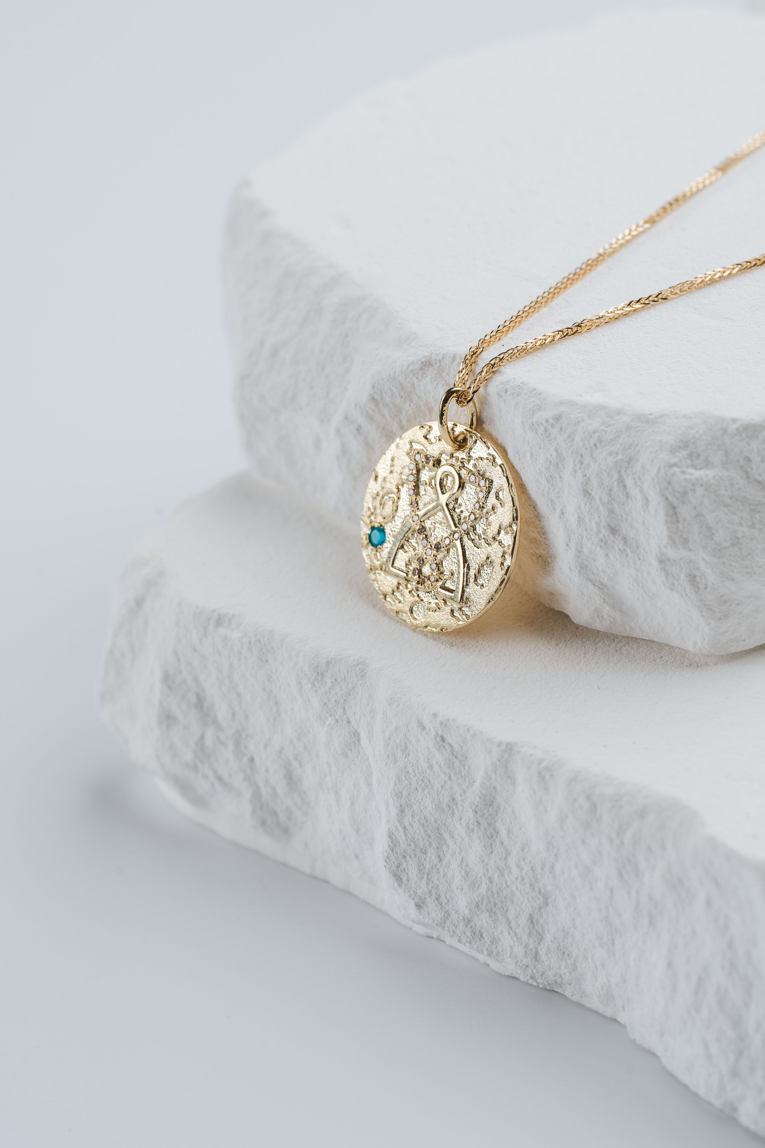 Delicate gold necklace with ornate pendant displayed on white stone surface.