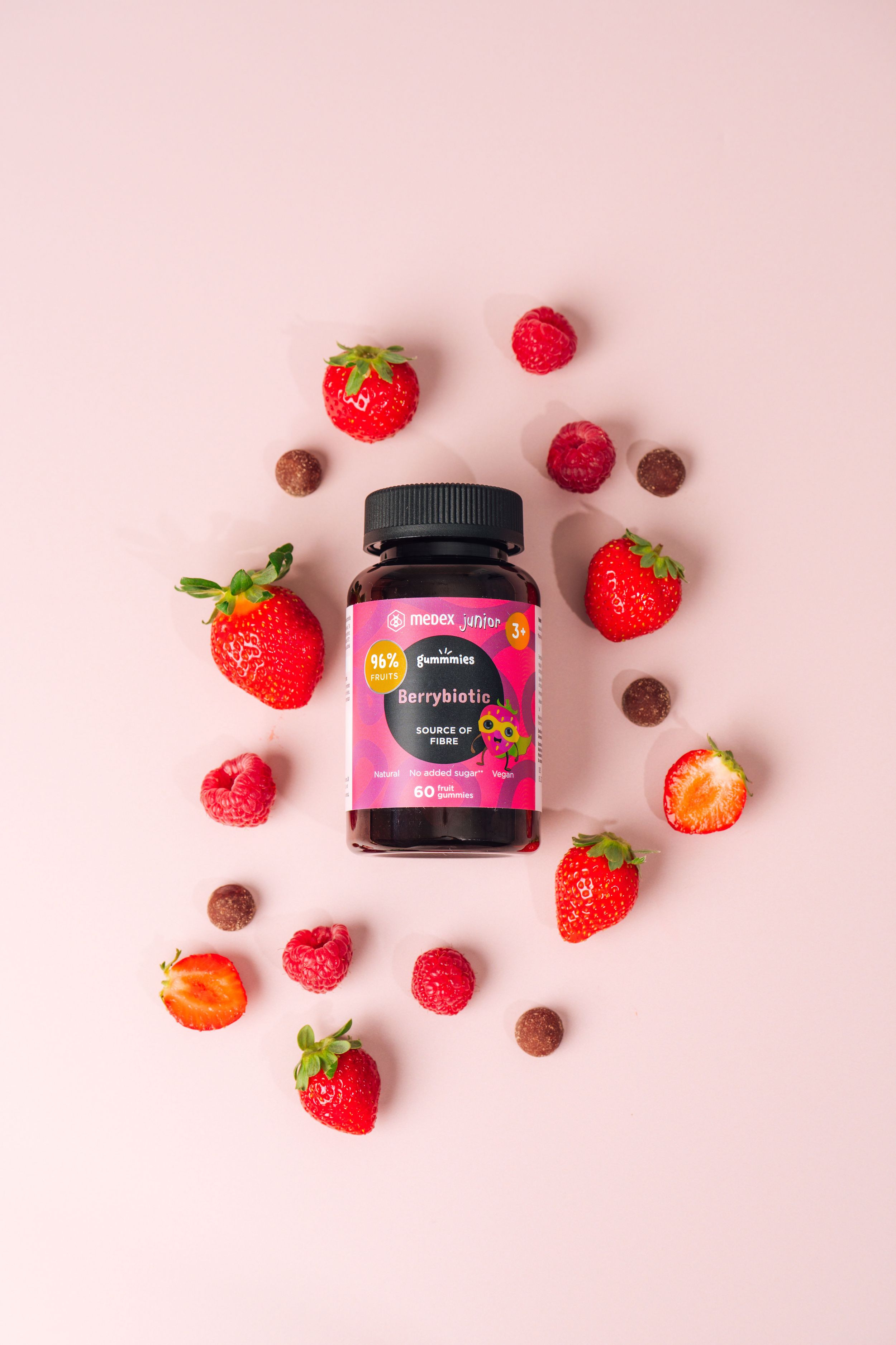 Beauty supplement container surrounded by fresh strawberries and chocolate pieces on pink surface.