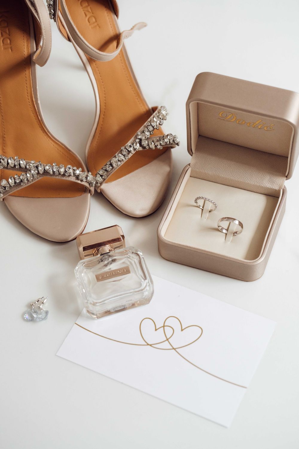 Elegant bridal accessories including sparkly heels, perfume bottle, and jewelry box on white background.