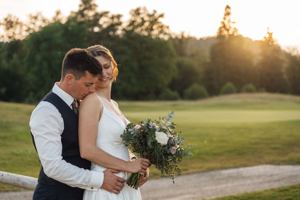 Romantic sunset portrait of newlyweds with bouquet on golf course.