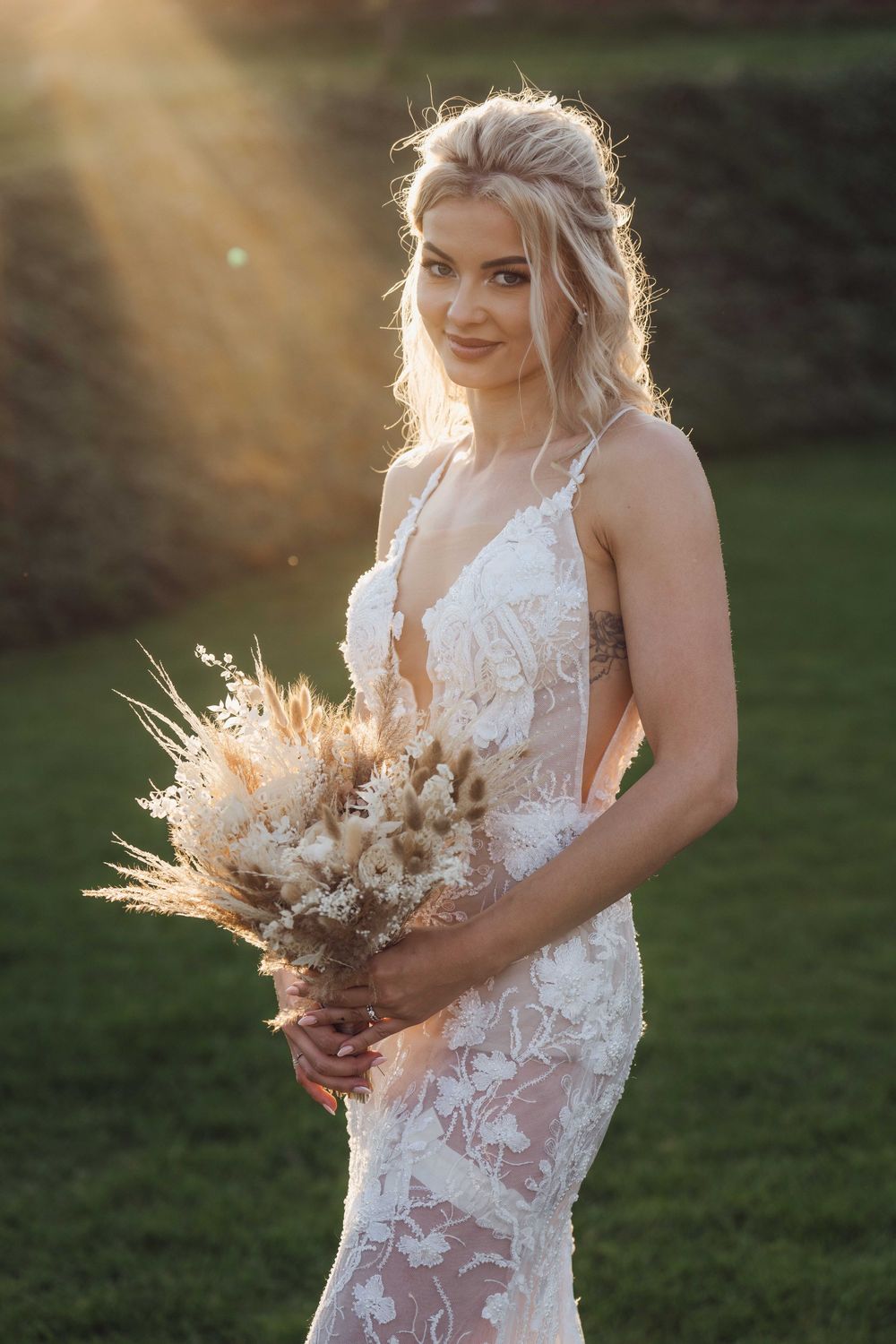 Bride holding dried flower bouquet in lace dress during sunset photo session.
