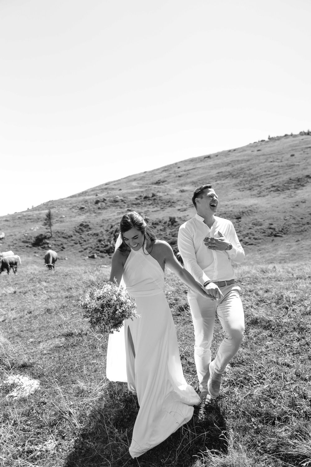 People in white attire walking through a grassy mountain meadow on a sunny day.