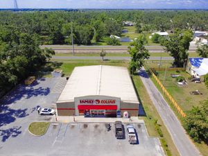 Aerial view of a Family Dollar retail store building with parking lot surrounded by green trees and roads in a rural area.