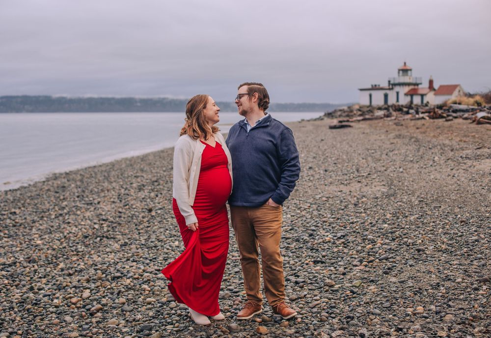 Couple walks along rocky shoreline with lighthouse visible in distance. Fedore Photography Spokane Liberty Lake Photographer Senior