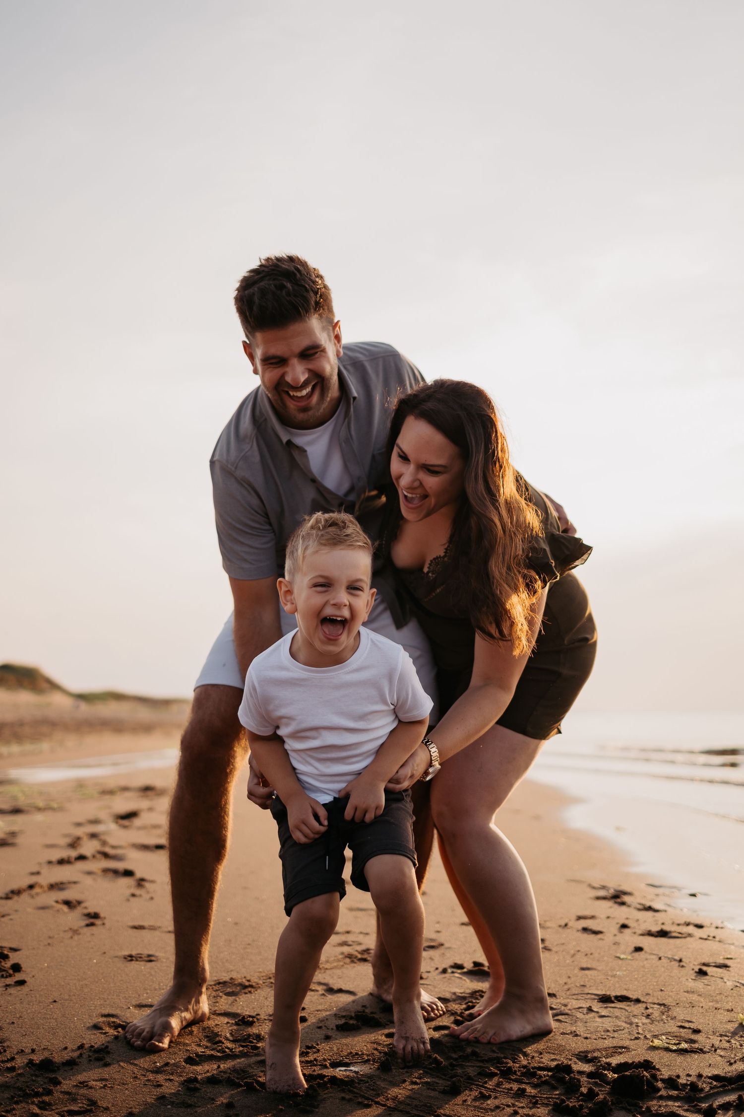 Happy family playing together on sandy beach at sunset.