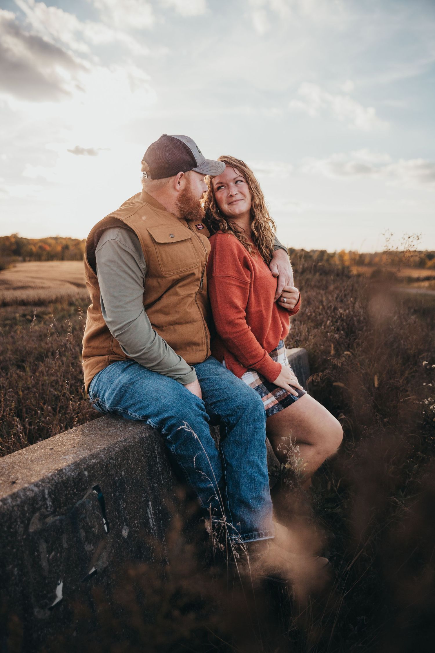 Couple sitting together on concrete ledge during sunset in rural setting.