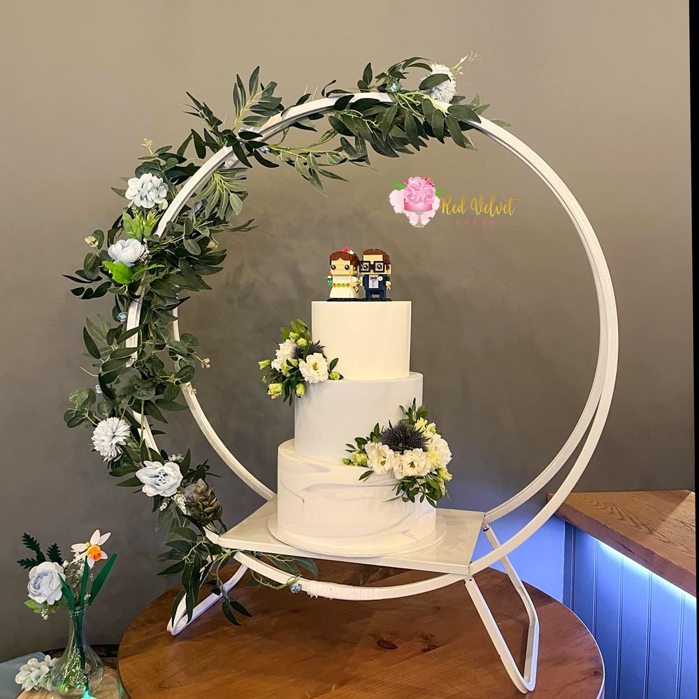 3 tier wedding cake finished in white and bluebell blue, on a white cake hoop stand and finished with fresh white roses and green leaves