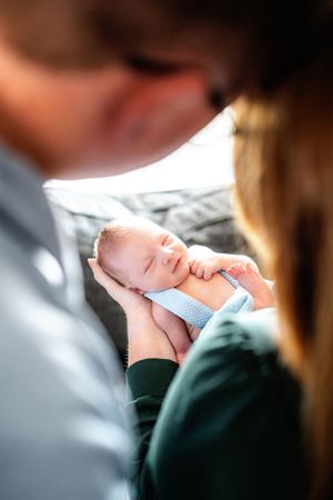 A newborn baby in blue sleeps peacefully while being held.