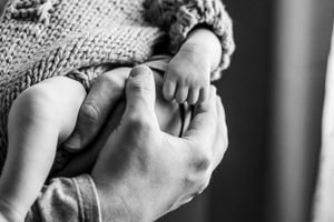 A black and white close-up of hands tenderly holding a baby.