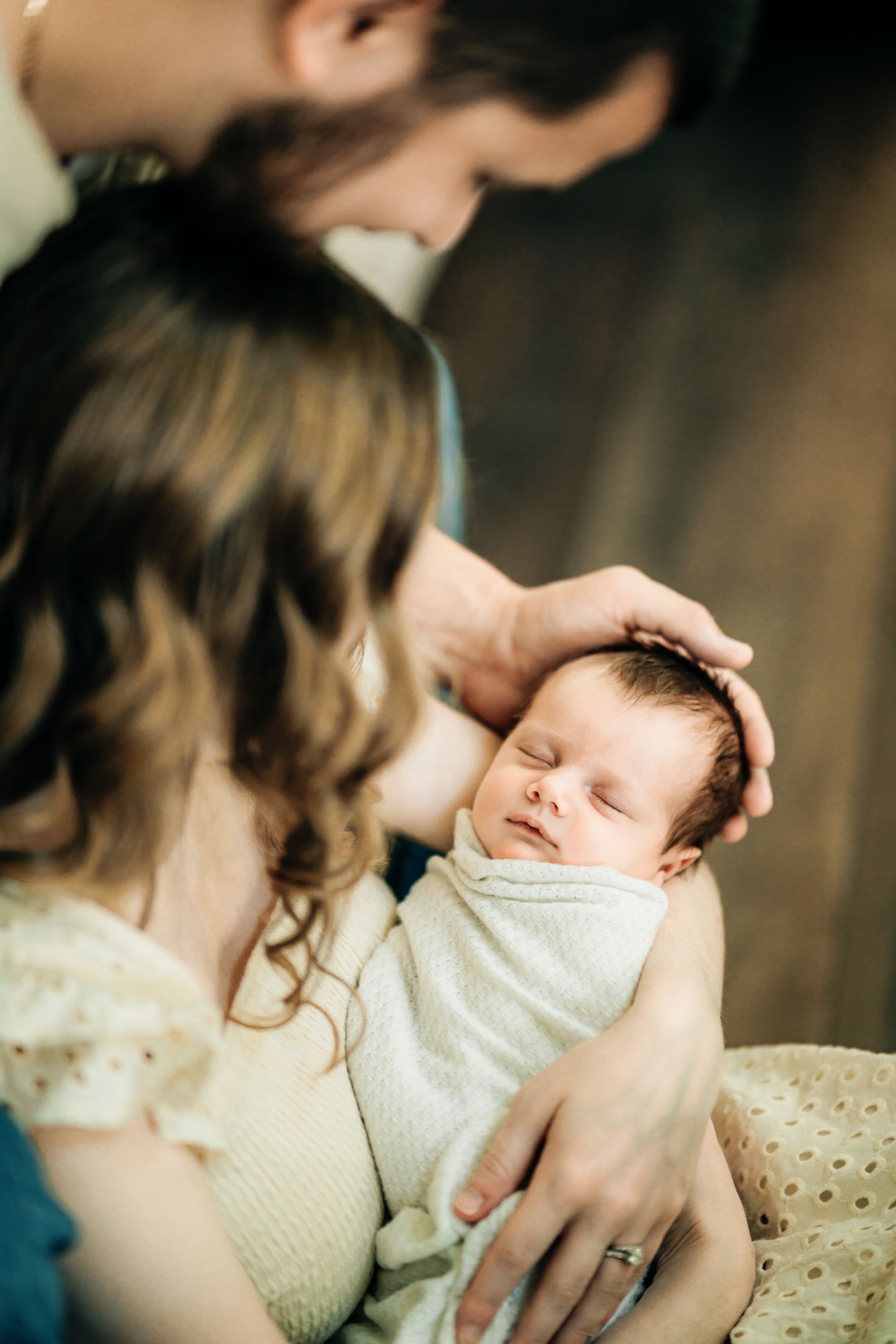 Close-up shots of parents lovingly cradling their sleeping newborn in soft white clothing.