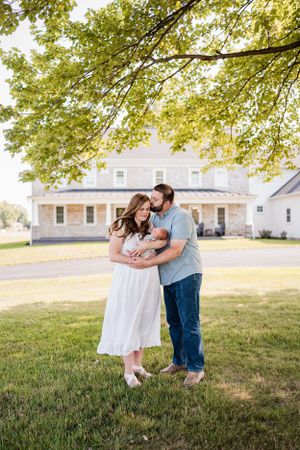 A tender family moment outside a white farmhouse on a sunny day.