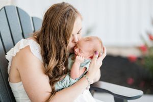 Tender motherly moment in a white Adirondack chair outdoors.