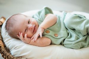 Sweet newborn baby in mint green outfit lying peacefully in woven basket.