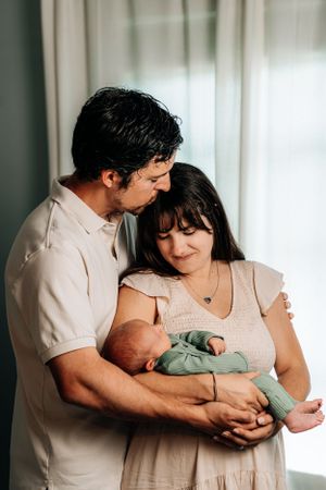Tender indoor family portrait with newborn baby wearing mint green outfit.